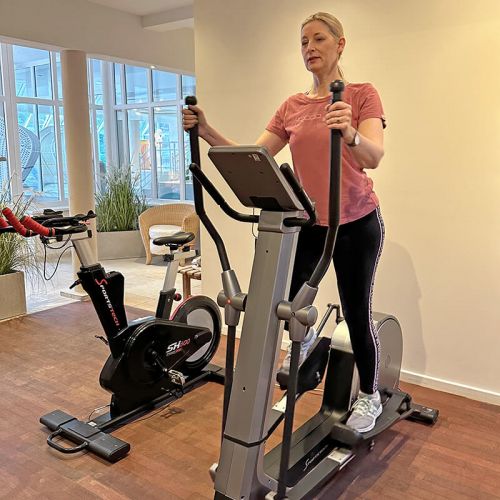 Wellness und Spa Hohe Wacht, Fitnessbereich, Frau ain Sportkleidung auf einem Stepper, links daneben Ergometer