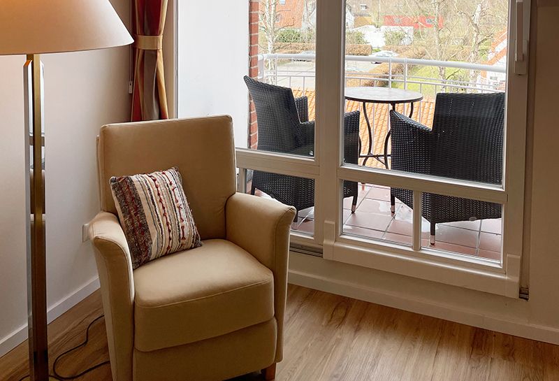 Doppelzimmer mit Loggia, auf der Loggia zwei Sessel und ein kleiner runder Tisch, Blick zur Süd-Westseite, vor der Loggiatür steht ein Lesesessel mit Kissen, daneben eine Stehlampe