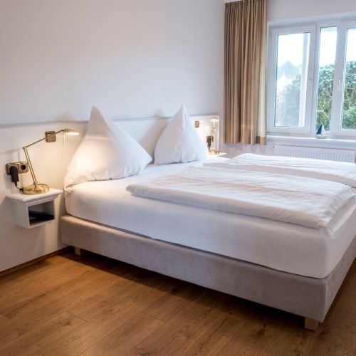 1-Zimmer-Ferienwohnung Schlafbereich mit Boxspringbett an der Wand zum Fenster hin, links und rechts daneben Nachtisch mit Licht