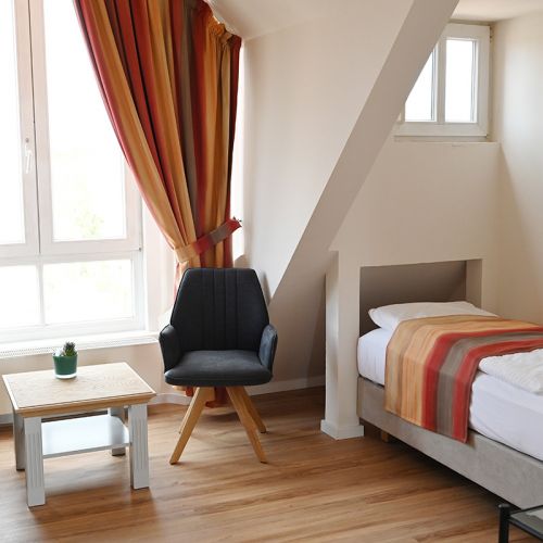 Schlafzimmer in Kurpark-Suite, rechte Seite Bett, links daneben Fenster, davor Sitzmöglichkeit mit Tisch