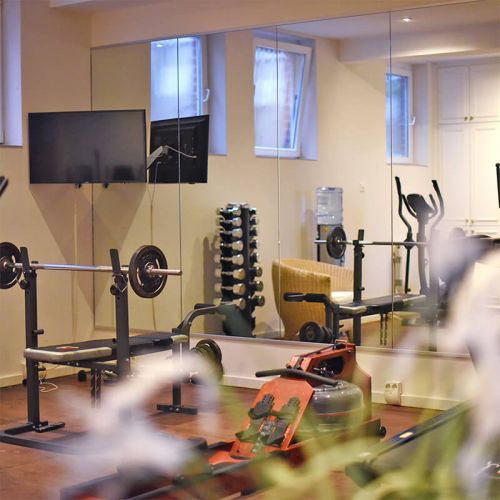 Wellness und Spa Hohe Wacht, Fitnessbereich, Spiegelfront, Fitnessgeräte spiegeln sich, Hantelbank mit Gewichten, Rudergerät, TV-Gerät hängt an der Wand
