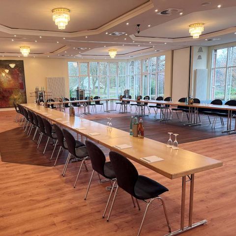 Tagungsraum im Hotel Hohe Wacht, Tische in Stühle in U-Form aufgestellt, eingedeckt mit Gläsern, Getränken und Schreibblöcken, an der Decke Kronleuchter, helle Fensterfront