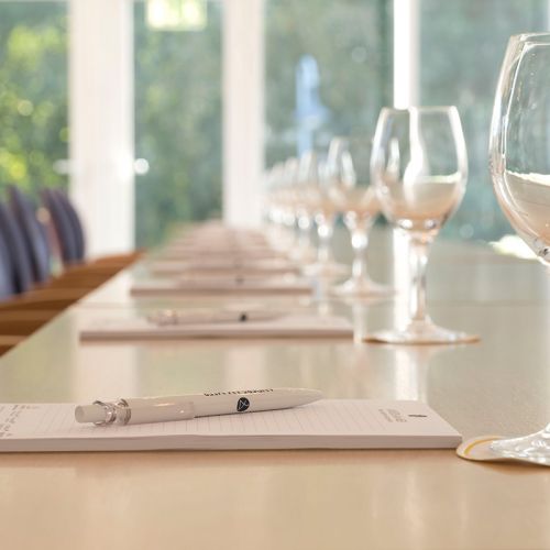 Tagungsraum Hotel Hohe Wacht, Nahaufnahme Tisch eingedeckt mit Schreiblöcken, Kugelschreiber und Trinkgläsern, Hintergrund Fenster