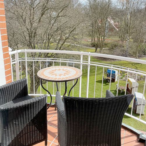 Loggia Doppelzimmer, auf der Loggia Sitzmöglichkeiten sowie ein runder Tisch, Blick in den Kurpark, im Kurpark stehen Bäume und Strandkörbe