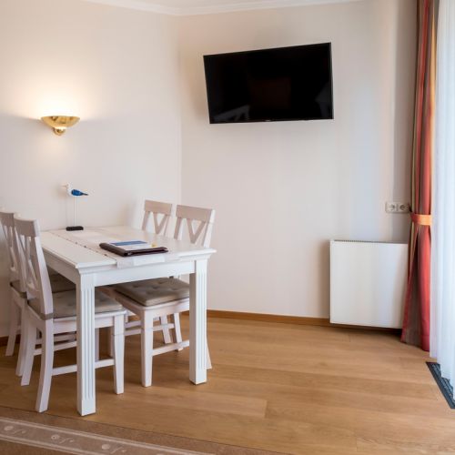 2-Zimmer-Komfortappartement Essbereich, Laminatboden, Esstisch mit vier Stühlen, an der Wand Lampe und TV-Gerät