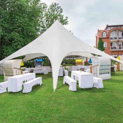 Kurpark Hotel Hohe Wacht, offener Pavillion, unterm Pavillion weiß bezogene Tische und Bänke, Strandkörbe als Sitzgelenheiten, Wimpelgirlanden, im Hiontergrund Rückansicht Hotel Hohe Wacht
