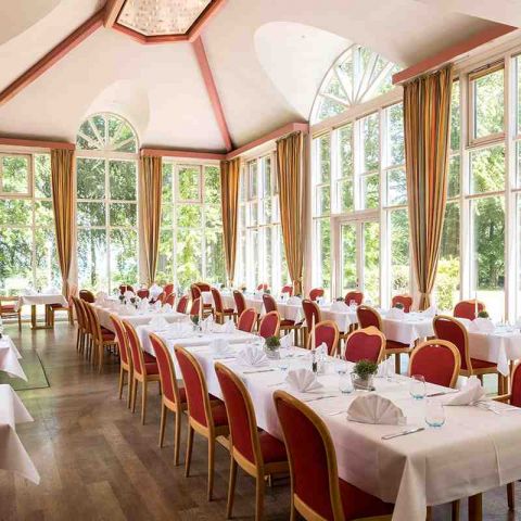 gedeckte Tafeln im Parkrestaurant am Fenster, mit Teller, Besteck, Wassergläser, Kerzen, gefaltete Servietten, Blick in den Kurpark