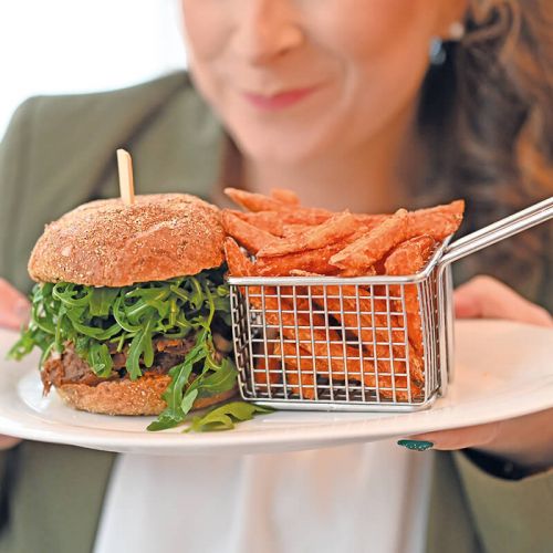 Speisekarte Parkrestautrant Hohe Wacht, Frau verschwommen und angeschnitten hält im Vordergrund Teller mit Pulled Pork Burger, Rucola und Süßkartoffelpommes