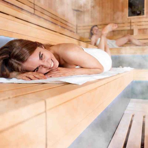 Wellness und Spa Hohe Wacht, zwei liegende Frauen mit Handtuch um den Körper in Sauna auf Holzbänken, Dampf schwebt in der Luft