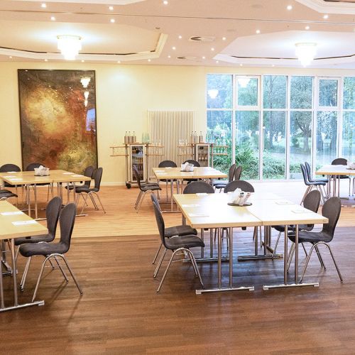 Tagungsraum Schleswig-Holstein im Hotel Hohe Wacht, Tische und Stühle in Blockform, auf den Tischen Schrebblöcke, im Hintergrund Getränkewagen, Fensterfront, an der Wand Malerei im Rahmen