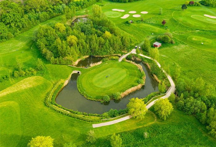 Luftaufnahme des Hohwachter Golfplatzes, Grün auf einer Insel im Teich, umgeben von Bäumen und Fairways