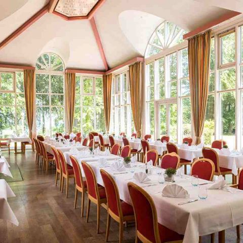 gedeckte Tafeln im Parkrestaurant am Fenster, mit Teller, Besteck, Wassergläser, Kerzen, gefaltete Servietten, Blick in den Kurpark