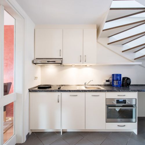 Küche in 2,5-Zimmer-Ferienwohnung mit Blick auf Küchenzeile, Herd mit Dunstabzughaube, Spüle, Backofen, Wasserkocher, Kaffeemaschine, Hängeschränke, rechts oben im Bild Treppe ins Obergeschoss