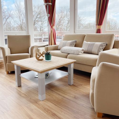 Sitzbereich Ostseesuite direkt an der Fensterfront, Sofa mit Kissen und Decke, zwei Sessel sowie Tisch mit Deko Anger und Pflanze