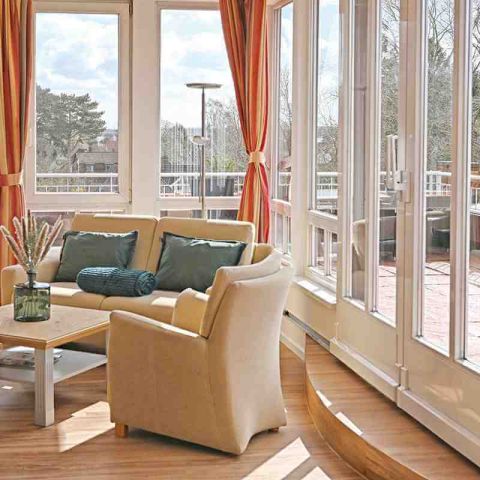 Ecke Wohnbereich Suite mit Couch, Sessel und Tisch, rundherum Fensterfront, Blick nach draussen auf den Balkon, Blick auf den Kurpark und die Ostsee