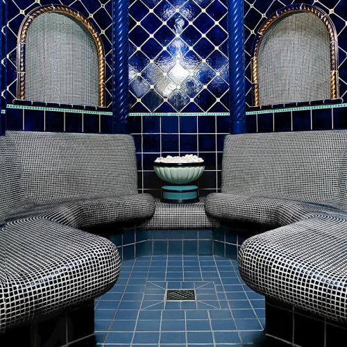 Wellness und Spa Hohe Wacht, blau geflieste Dampfsauna, Sitzflächen mit schwarzen kleinen Mosaikfliesen, in der Mitte am Boden Abfluss, an der Wand heiße Steine