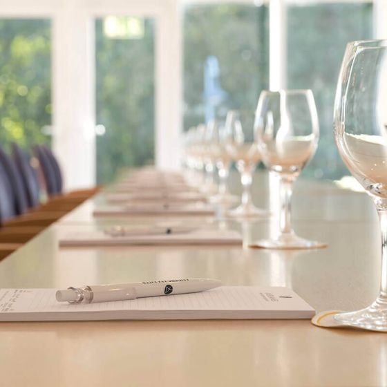 Tagungsraum Hotel Hohe Wacht, Nahaufnahme Tisch eingedeckt mit Schreiblöcken, Kugelschreiber und Trinkgläsern, Hintergrund Fenster