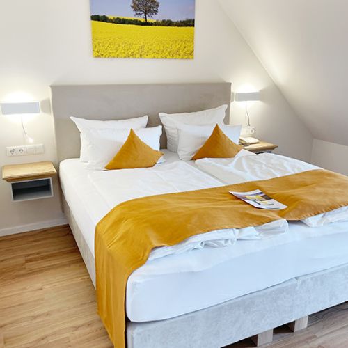 Schlafbereich im Turmzimmer, Boxspringbett mit Kopfende an der Wand, darüber Leinwand mit Rapsmotiv, links und rechts vom Bett Lampen und Ablageflächen