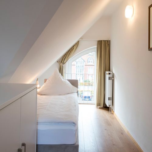 2. Schlafzimmer in einer 2,5 Zimmer Ferienwohnung, ein schmales Bett unter der Schräge, davor steht ein Schrank, geradaus durch Fenster, rechts Heizungskörper an der Wand