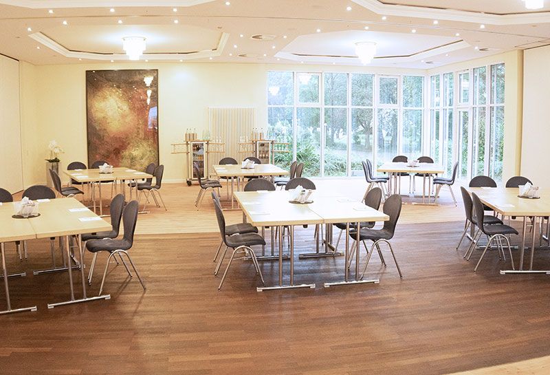 Tagungsraum Schleswig-Holstein im Hotel Hohe Wacht, Tische und Stühle in Blockform, auf den Tischen Schrebblöcke, im Hintergrund Getränkewagen, Fensterfront, an der Wand Malerei im Rahmen