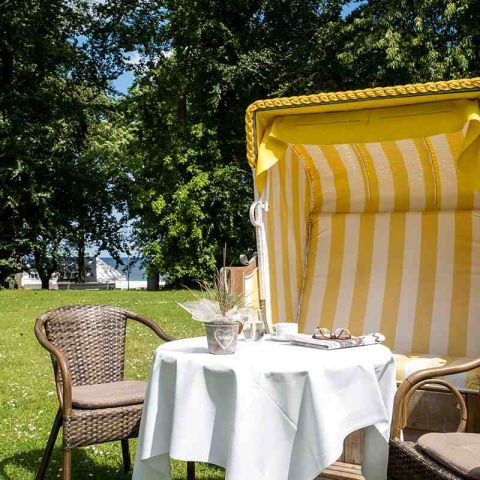 Kurpark Hotel Hohe Wacht, Strandkorb mit Tisch und zwei Rattanstühlen, weiße Tischdecke, auf dem Tisch Kaffeegedeck, Zeitschrift, Brille, Blumentopf, im Hintergrund Blick auf die Ostsee