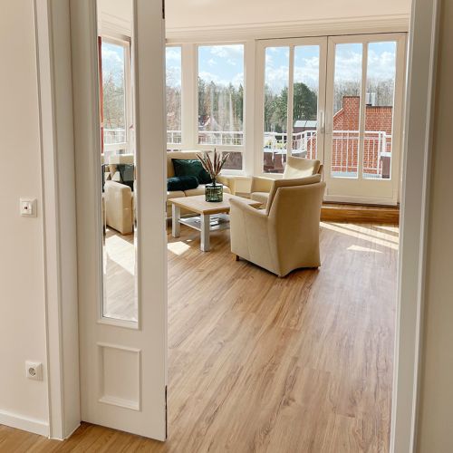 Kurpark-Suite Eingangsbereich, Durchgang zum Schlaf- und Wohnbereich, Blick auf die Sitzecke mit Sofa, Sessel und Tisch, hinter der Sitzecke Fensterfront mit Terrassentür zum Balkon