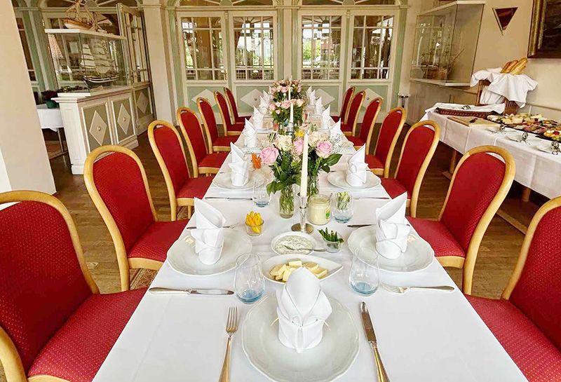 gedeckte Tafel im Raum Perle im Hotel Hohe Wacht, eingedeckt mit Teller, Besteck, Gläser, gefaltete Servietten, Kerzen, Blumenvasen mit Rosen, rechts an der Wand Tisch mit Buffet, verschiedene Platten, Baquettestangen