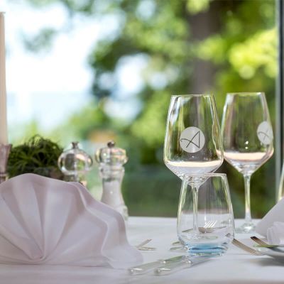 Nahaufnahme gedeckter Tisch im Parkrestaurant am Fenster, mit Teller, Besteck, Wasser- und Weingläser, Kerze, Salz-und Pfefferstreuer, gefaltete Servietten, Blick in den Kurpark auf die Ostsee