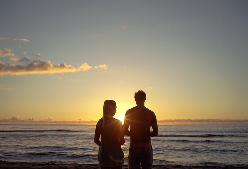 Sonnenuntergang am Strand, ein Pärchen steht mit dem Rücken zur Kamera und schaut über das Meer